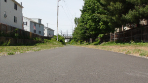 A picture of a paved bike path, with a neighborhood in the background, on a summer day.